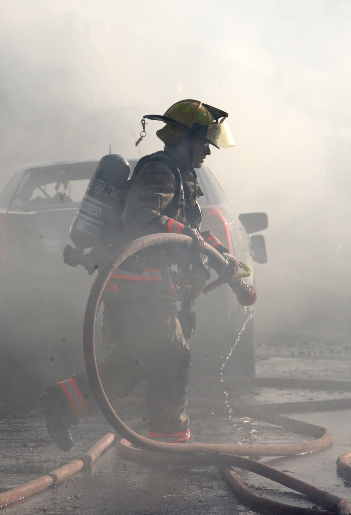 Firefighter carries hose through smoke